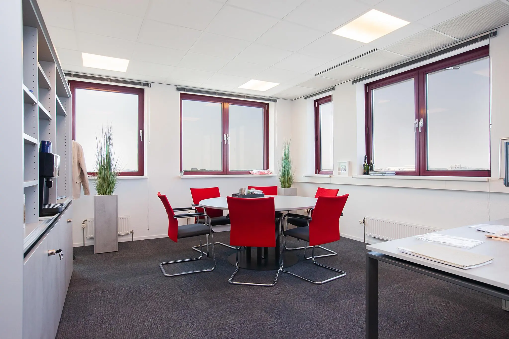 Modern kantoorinterieur aan de Laan der Verenigde Naties met vergadertafel, rode stoelen en grote ramen.